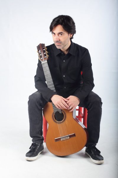 Diego Corraliza, profesor que imparte el curso de Armonía Moderna, sentado, con la guitarra entre las piernas y mirando de soslayo a la cámara